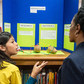 Child explaining their science fair poster to a teacher