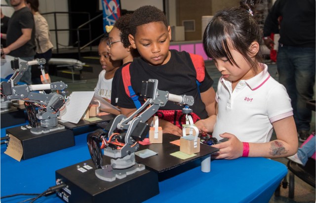 Young students look at a model of a robotic arm with STEM education. STEM (Science, Technology, Engineering, and Mathematics) education is a method of hands-on teaching and learning