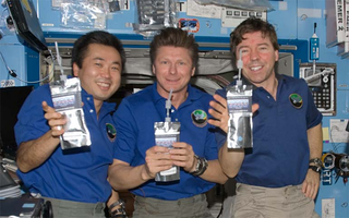 Three astroanuts holding water containers aboard the ISS