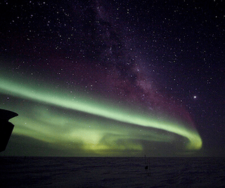 Pale green Northern Lights shimmer against a starry sky