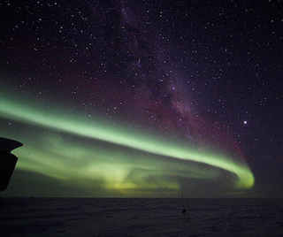 Pale green Northern Lights shimmer against a starry sky