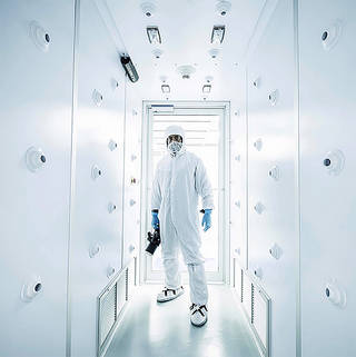 Chris Gunn wears a white clean room suit and holds a camera