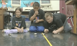Three children work with spools that spin on the floor