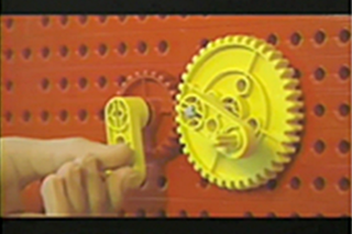 A hand turns a handle to move two gears