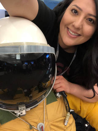 Jessica Arreola leans next to someone wearing a spacesuit and white space helmet