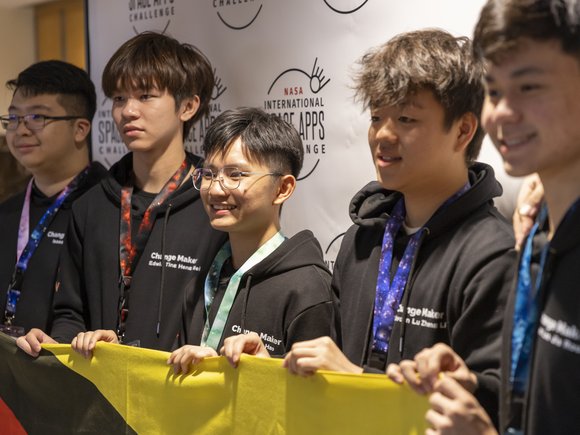 A group of 5 young men pose for a picture while holding a banner