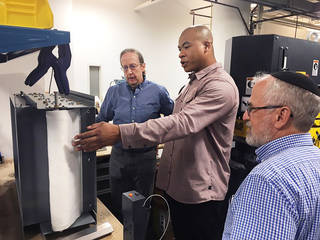 Three men in laboratory look at filter device sitting on table.