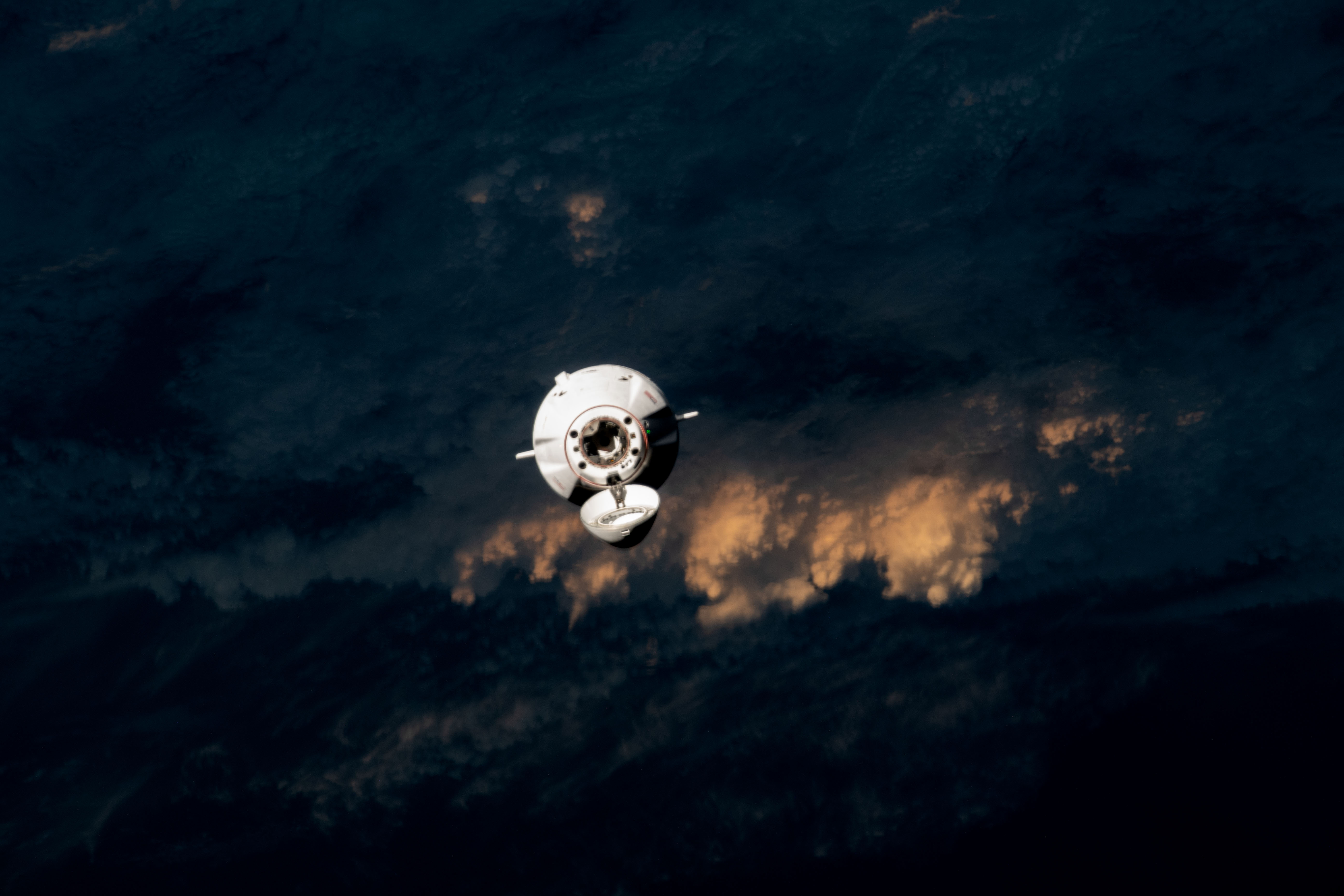 The last rays of an orbital sunset illuminate the cloud tops above the Pacific Ocean off the coast of Japan, providing a dramatic background for the SpaceX CRS-28 Dragon cargo craft as it approached the International Space Station for docking on June 6, 2023.