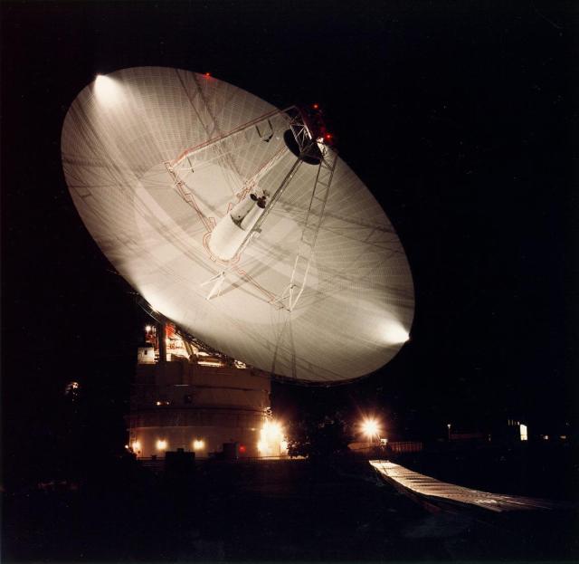 A giant 230-foot (70-meter) antenna lights up a dark night sky with golden hues.