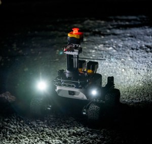 A small rover lights up some rocky terrain on Earth at night.