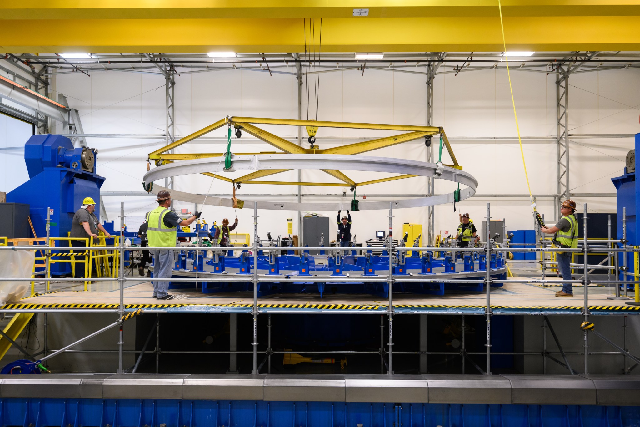 A crew of workers are working together to place a large circle object on top of a machine 