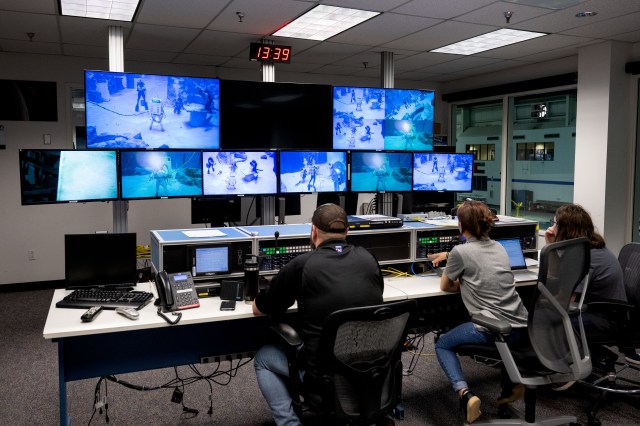 3 people sit in front of 9 screens watching divers in the Neutral Buoyancy Lab