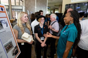 Two female students present their poster to a woman in a NASA shirt