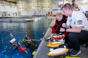 Two Micro-g NExT participants crouch at the edge of the Neutral Buoyancy Lab pool and speak to a diver