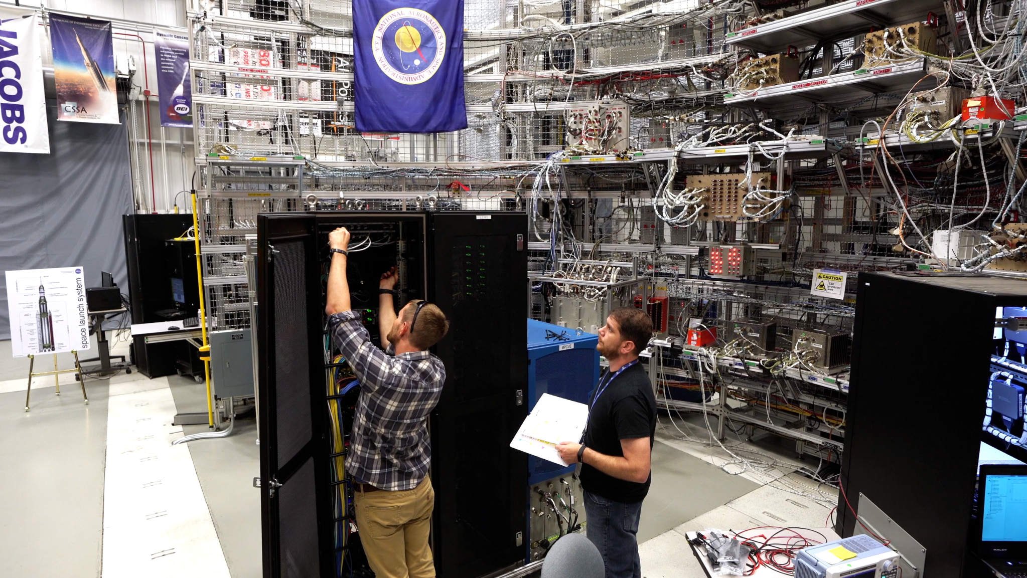 two men working on a large computer system surrounded by lots of cables