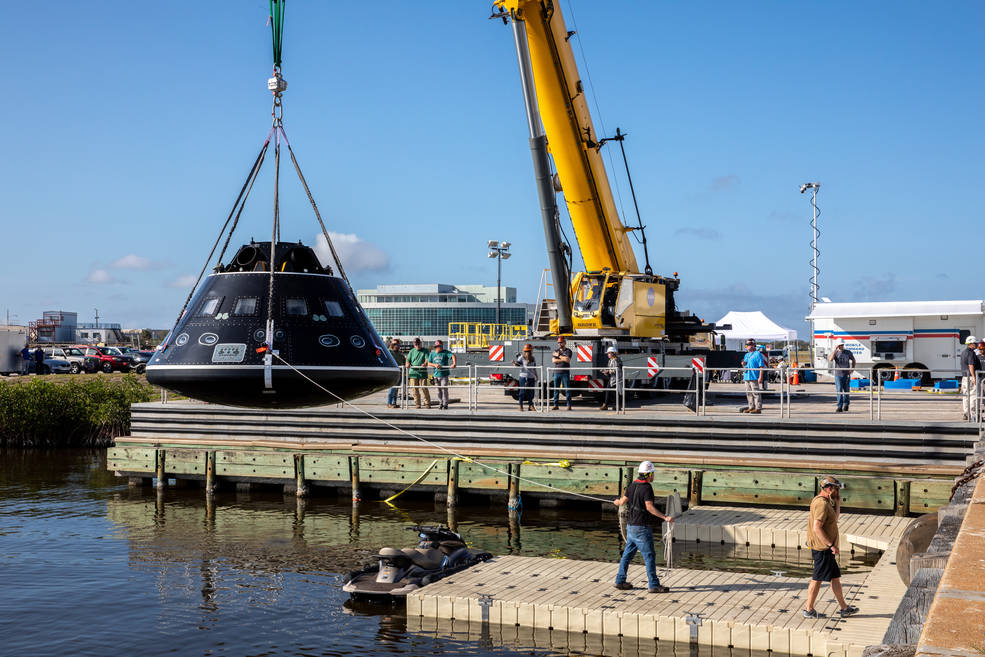 A crane holds a Crew Module Test Article, which is being used to practice Orion recovery operations, above the water at the turn basin in the Launch Complex 39 area at Kennedy Space Center in Florida.