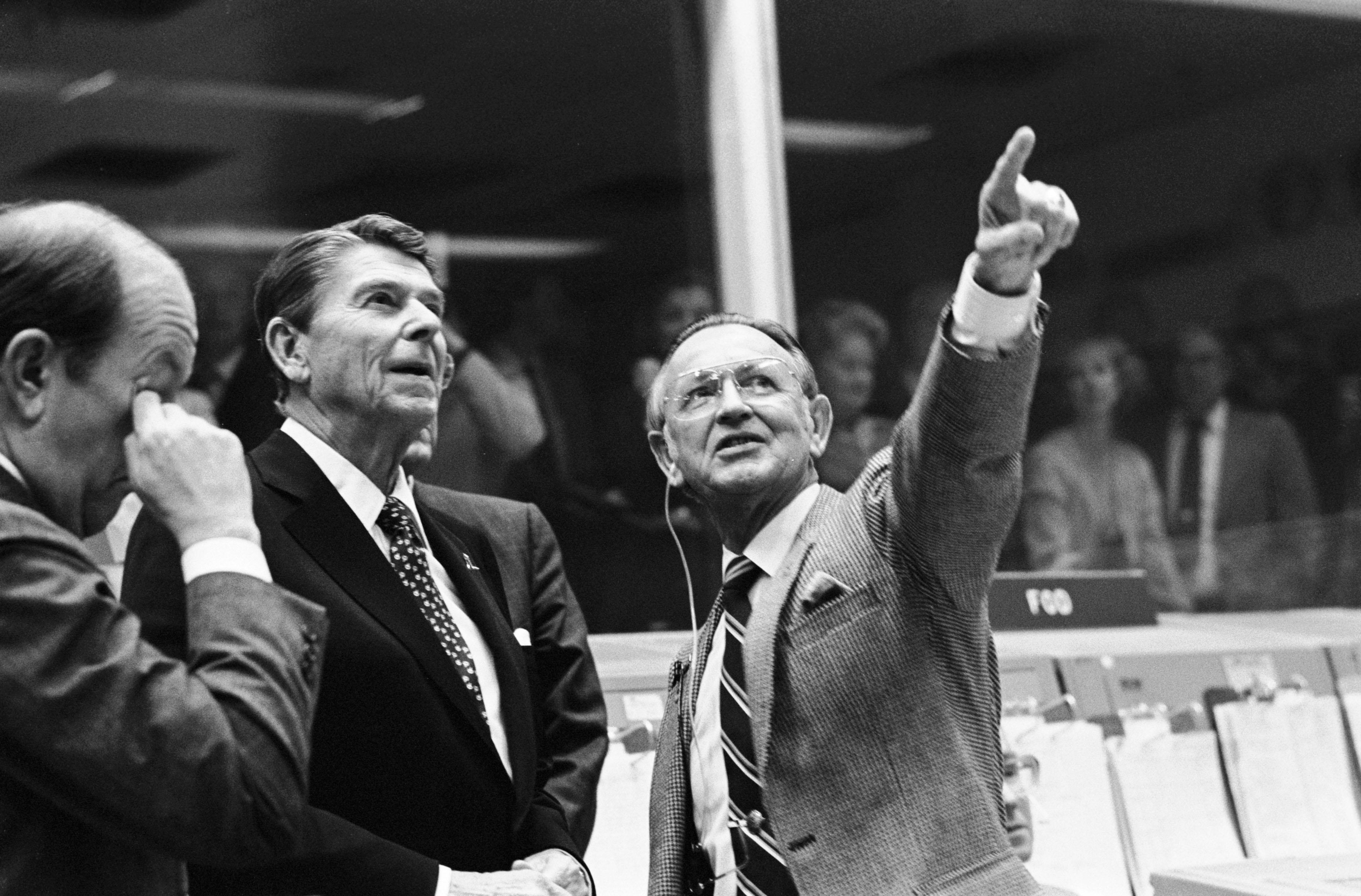 President Ronald Reagan is briefed by JSC Director Christopher C. Kraft Jr., who points toward the orbiter spotter on the projection plotter in the front of the mission operations control room in the Johnson Space Center's Mission Control Center