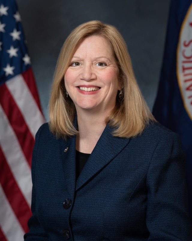 portrait of kathleen schubert with u.s. and nasa flags behind her.