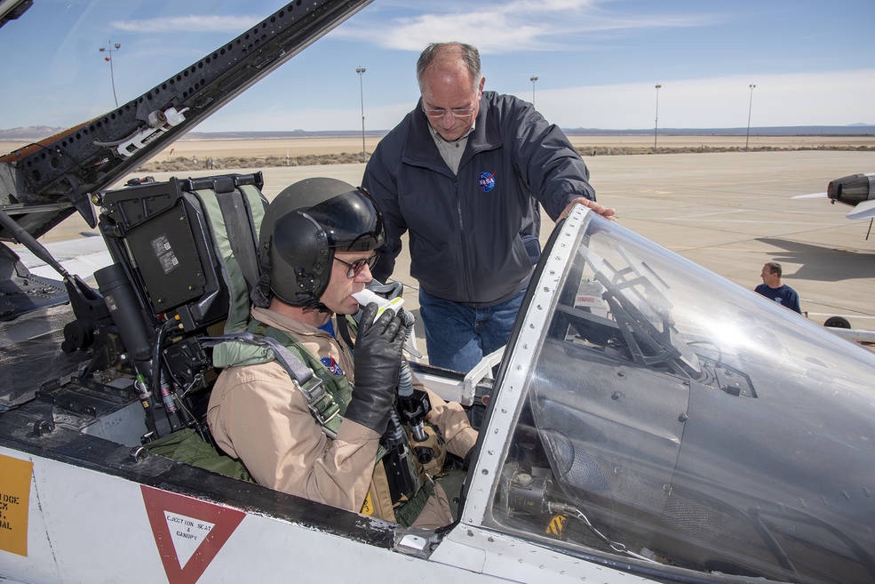 Pilot sits in a NASA aircraft with a man watching him take a breathing test.