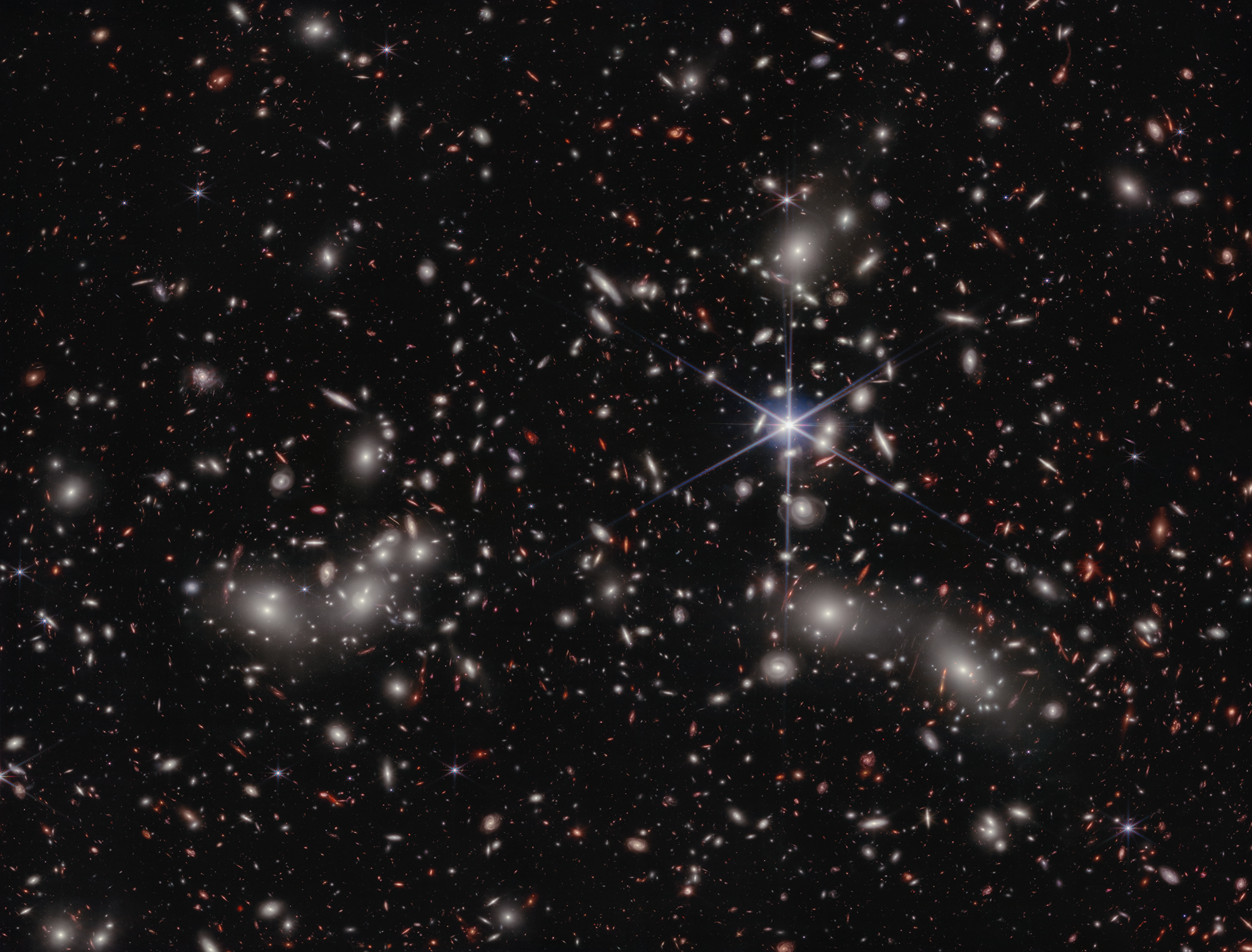 A crowded galaxy field on a black background, with one large star dominating the image just right of center. Three areas are concentrated with larger white hazy blobs on the left, lower right, and upper right above the single star.