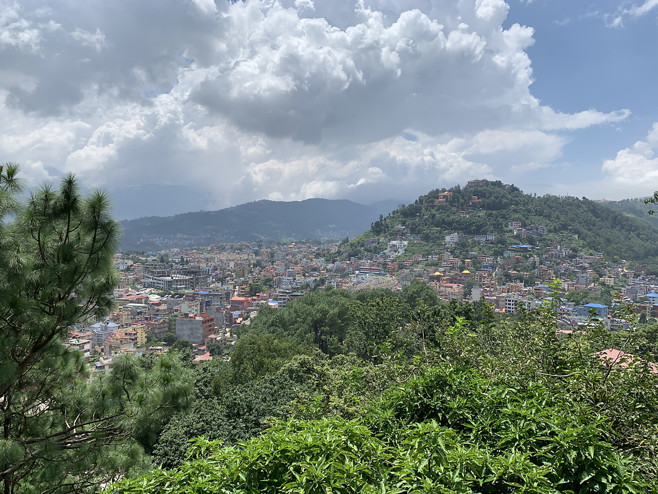 A mountainous view of Kathmandu, Nepal with green trees in the foreground and a multitude of buildings in the background.