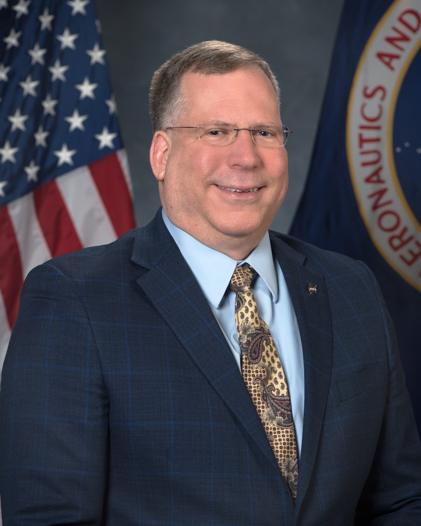 A portrait of Gib Winter smiling in front of the american flag.