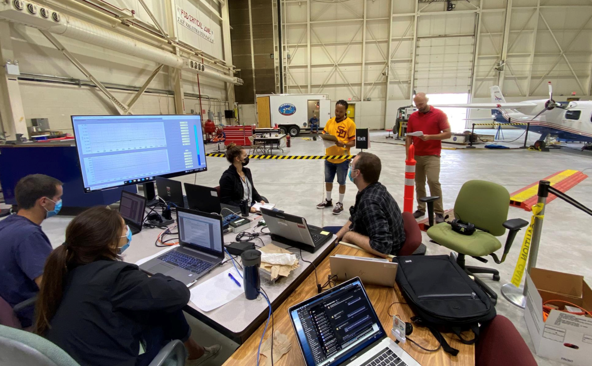 Several NASA personnel meeting in an aircraft hangar.