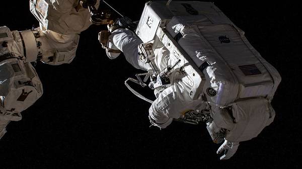 image of an astronaut standing on a robotic arm during a spacewalk