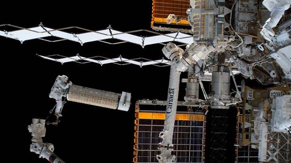 image of an astronaut holding on a rolled up solar panel during a spacewalk