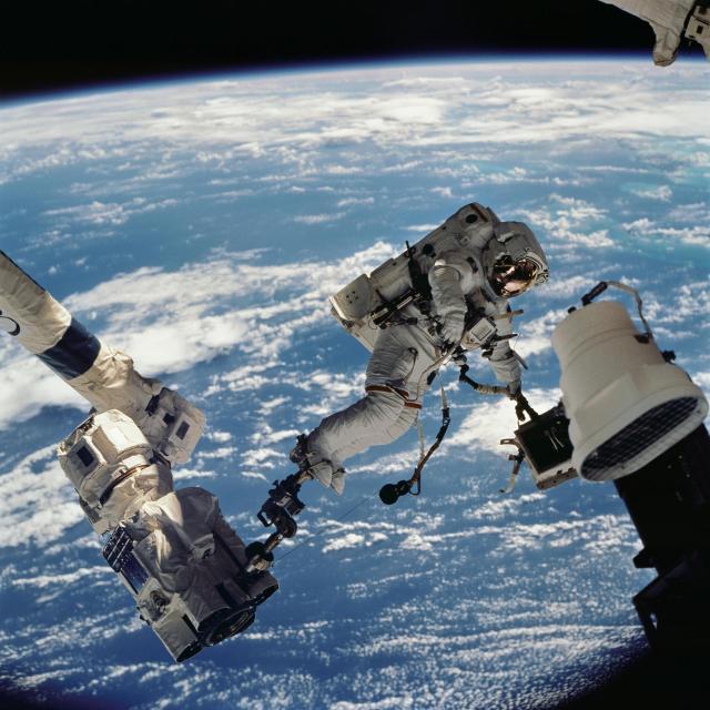 Astronaut David A. Wolf rides the Canadarm2 robotic arm during a spacewalk.