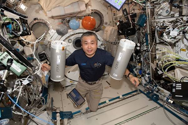 image of an astronaut holding silver cylinders while floating in the laboratory module