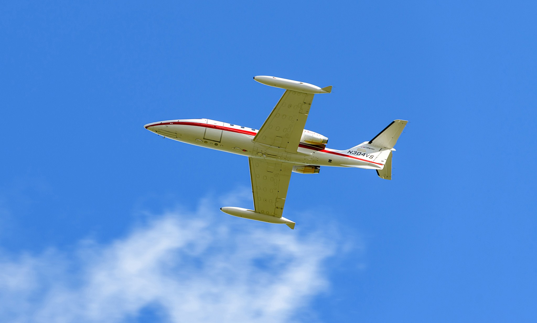 Bottom view of the Learjet 25 aircraft in flight against blue skies.