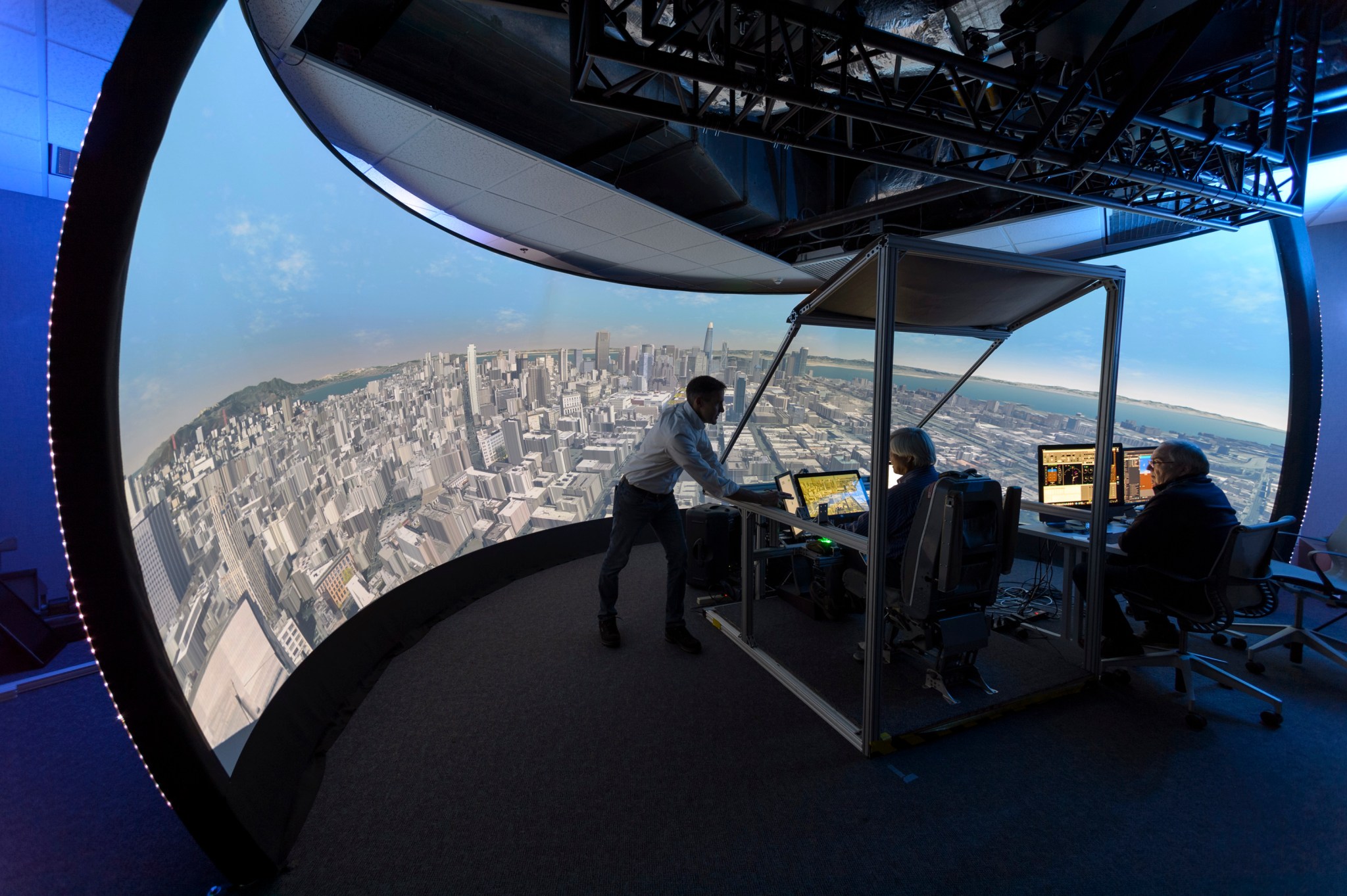 Inside a NASA simulation lab with a large screen simulation screen showing San Francisco city views and three workers in the center.
