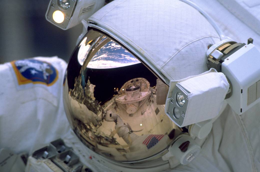 Closeup of astronaut on spacewalk with Earth and fellow spacewalker reflected in helmet visor
