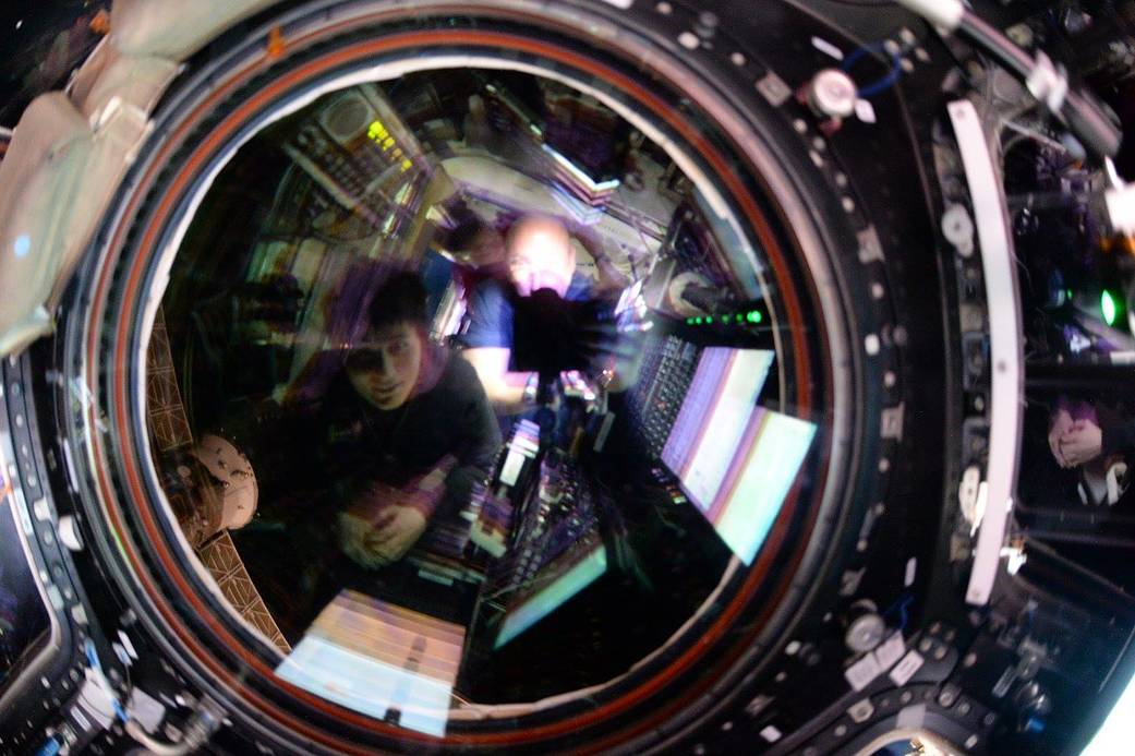 NASA astronaut Scott Kelly and ESA astronaut Samantha Cristoforetti reflected in circular lens watching spacecraft arrival 