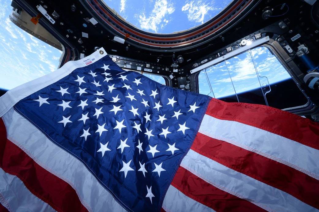 American flag in cupola of International Space Station with Earth visible through windows