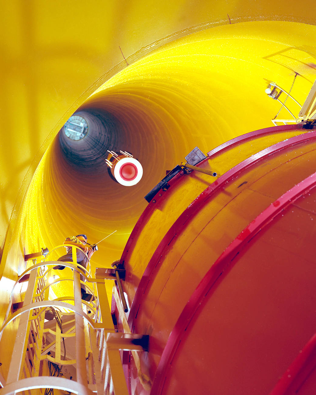 View from below looking up into bright yellow walled tunnel with object being lowered from top