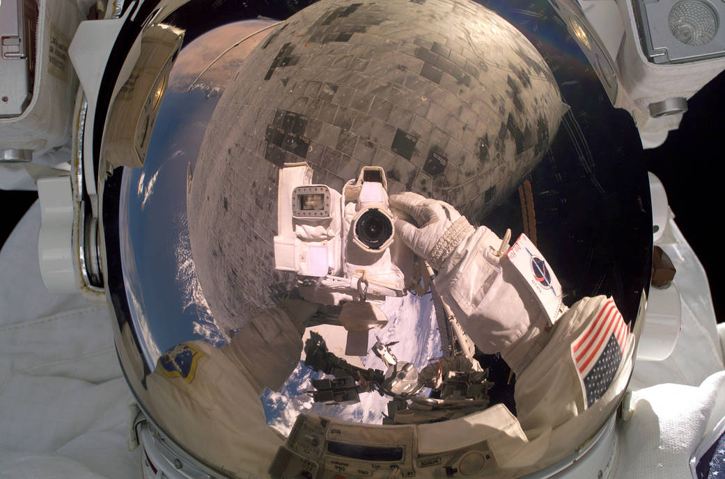 Closeup of astronaut's helmet visor with camera taking photo and shuttle tiles reflected