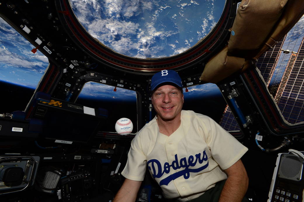 Astronaut Terry Virts wearing baseball cap, replica Jackie Robinson Dodgers jersey with baseball in space station cupola