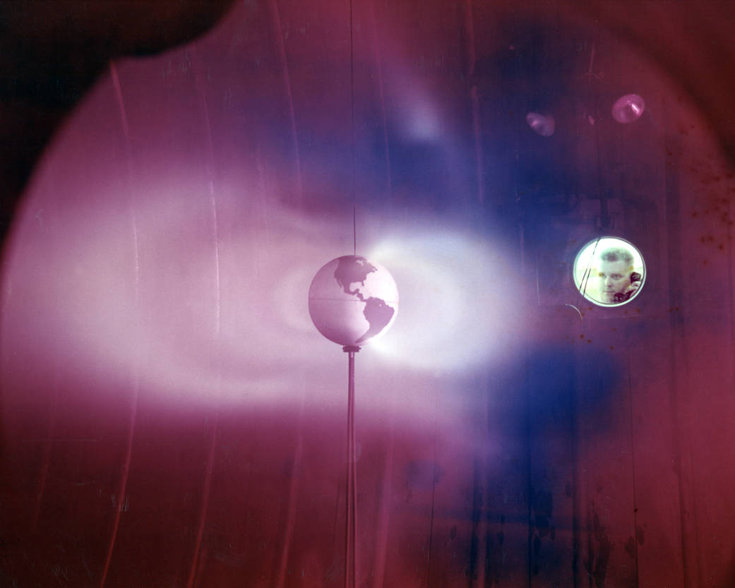 Model of Earth in large rose colored room with radiation simulation arcs, and technician looking through window
