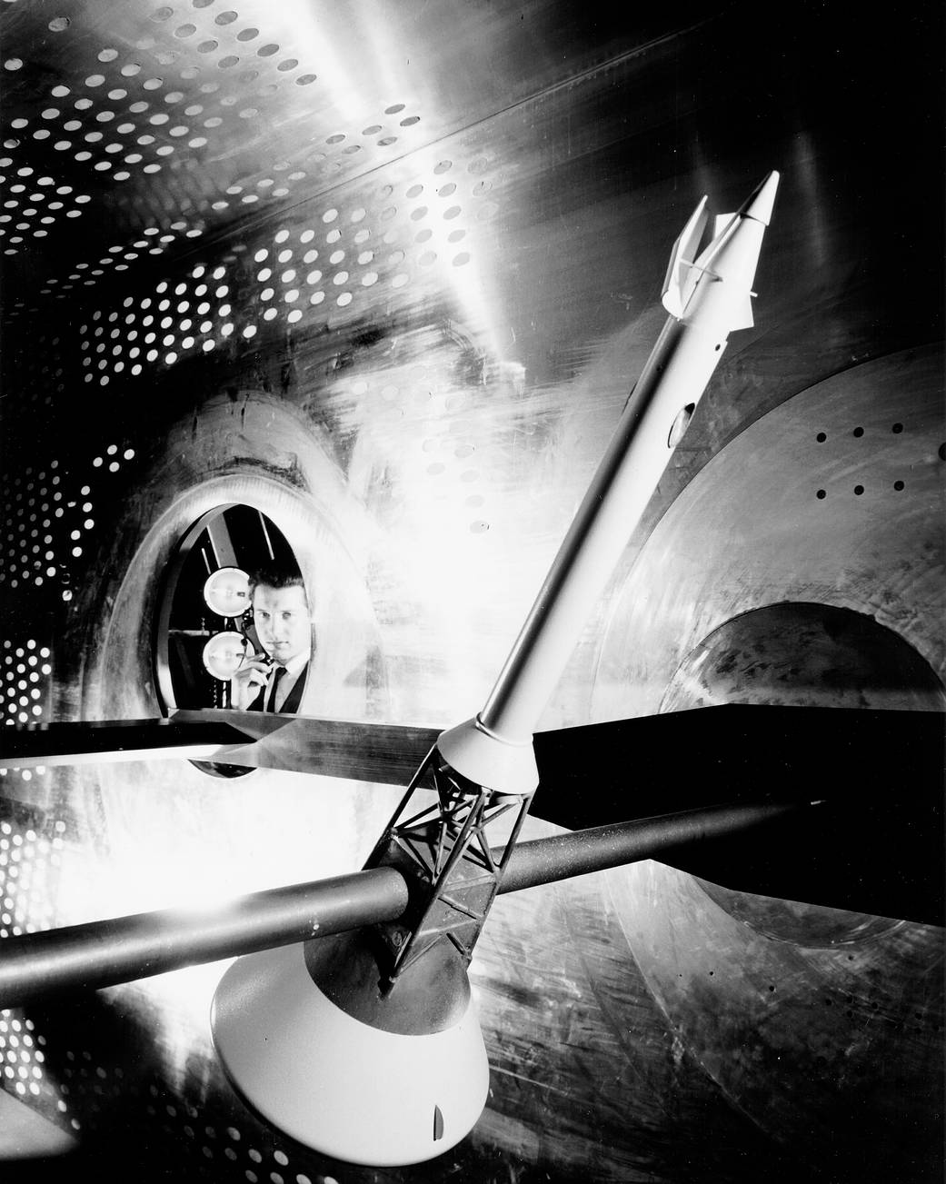 Black and white photograph of engineer looking into room with small Apollo capsule module