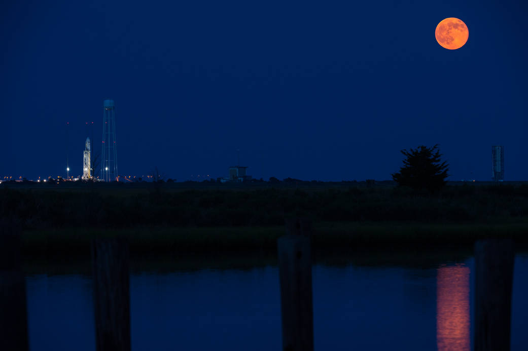 The full moon rises in the sky to the right of the Orbital Sciences Corporation Antares rocket, with the Cygnus spacecraft onboa