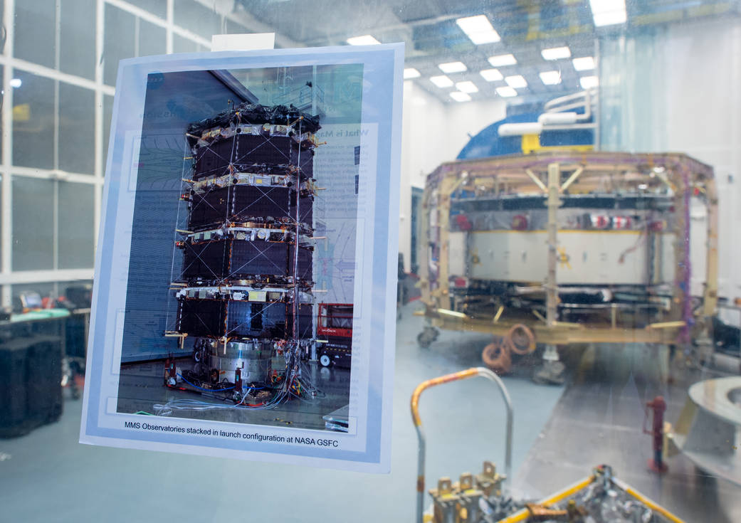 A photograph showing what all four Magnetospheric Multiscale (MMS) spacecraft look like when stacked is seen taped to the window