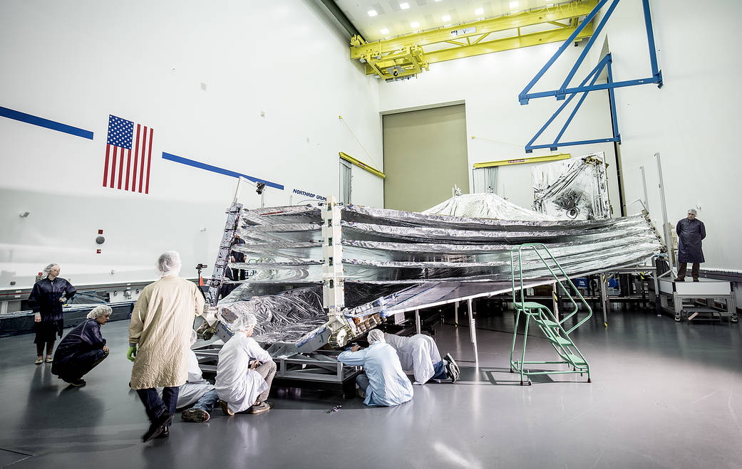 In this photo, engineers and scientists examine the sunshield layers on this full-sized test unit.