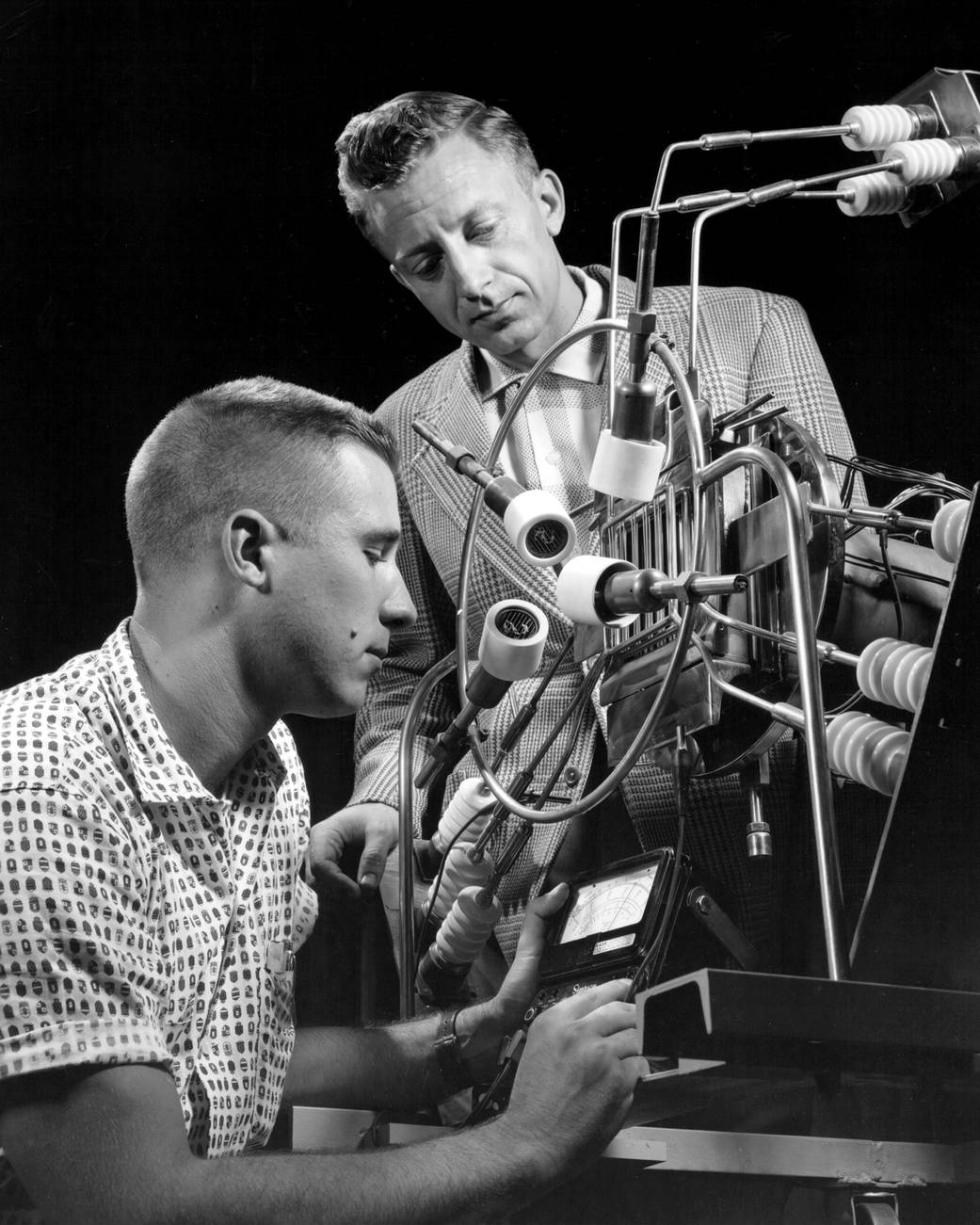 Black and white photo of two men looking at small engine