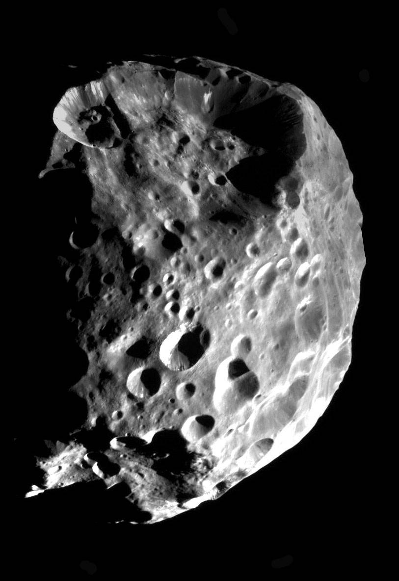 Closeup view in black and white of heavily cratered, irregularly shaped moon