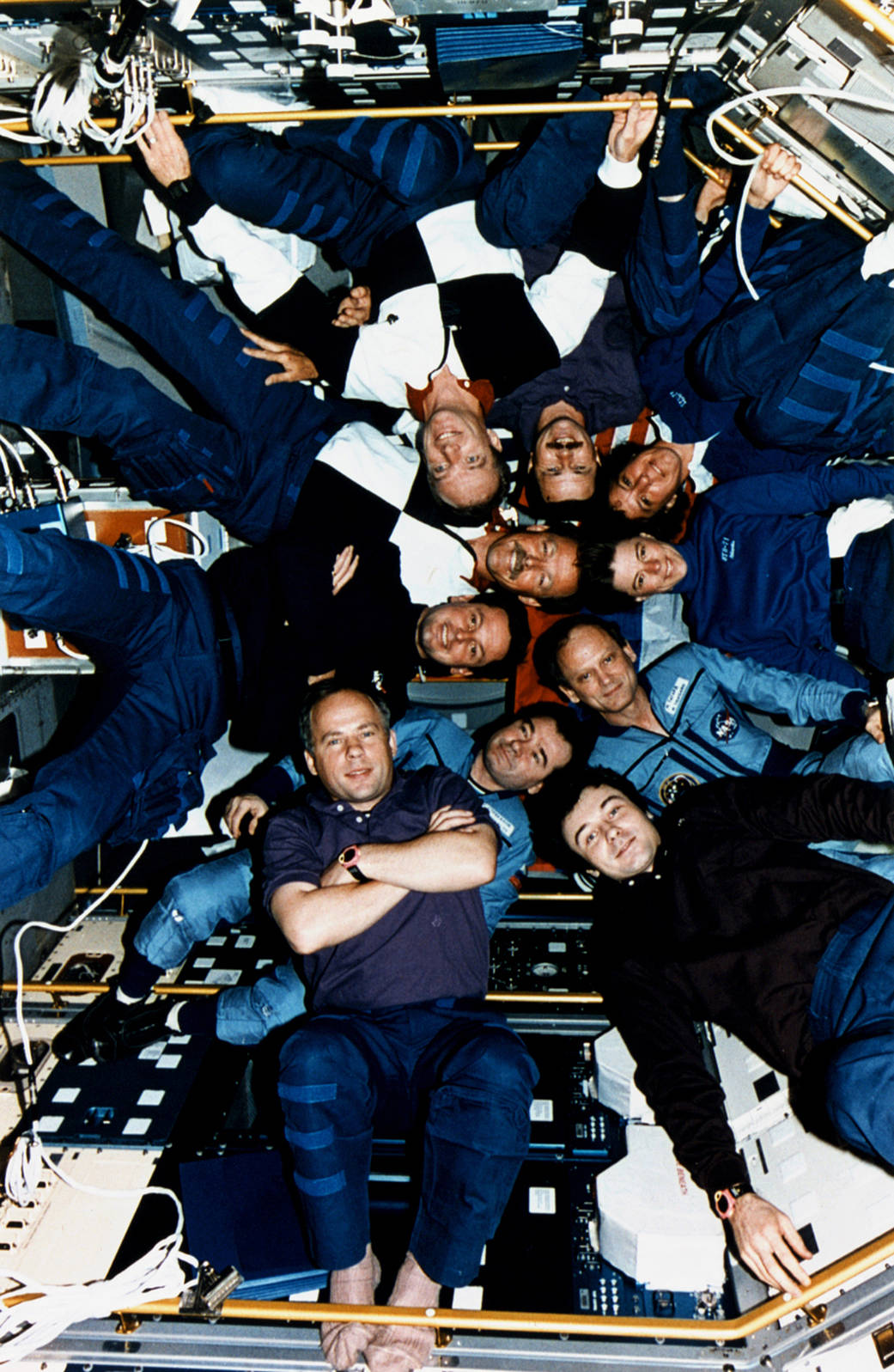 Ten astronauts and cosmonauts pose in circle inside Spacelab module