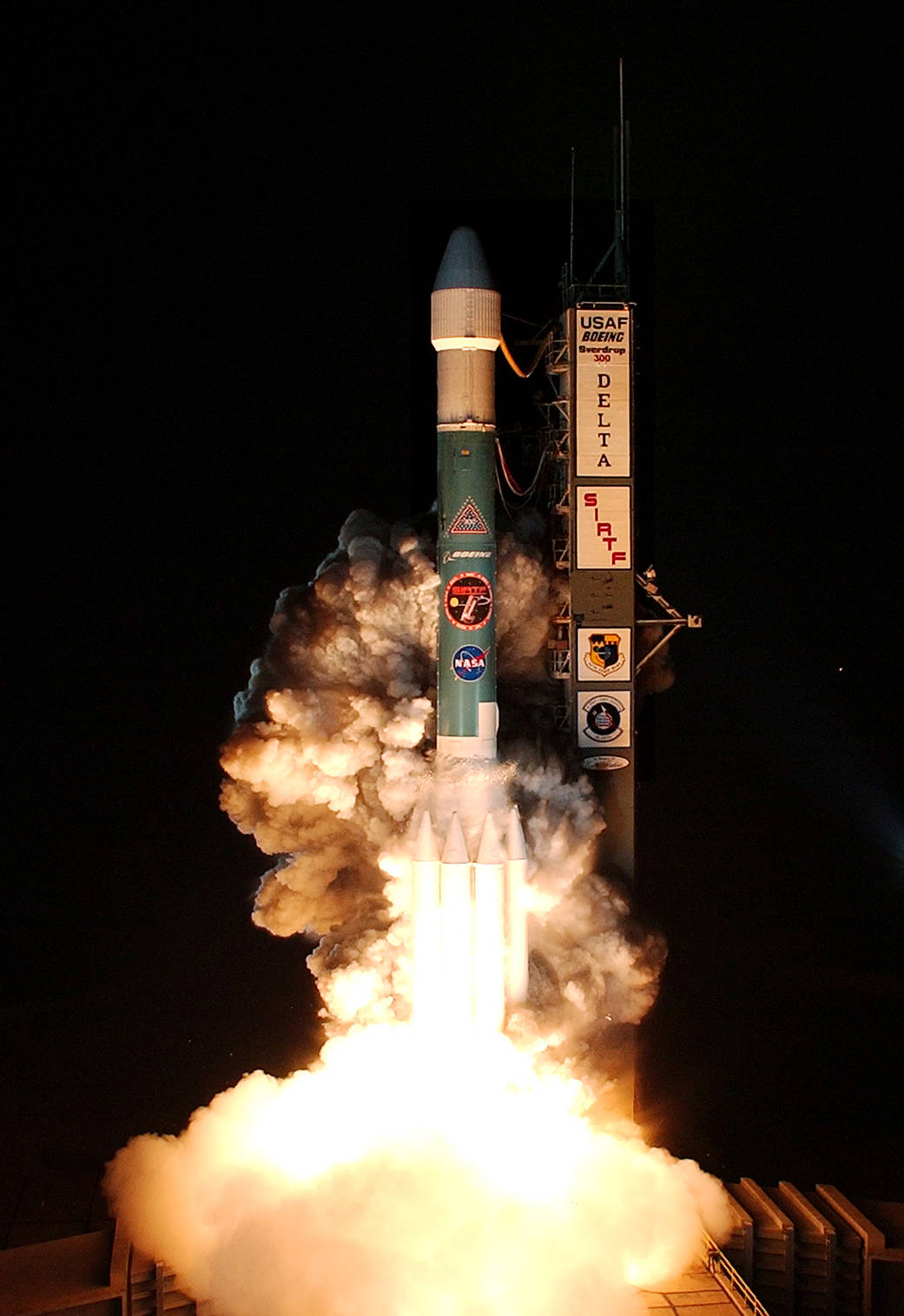 Closeup image of nighttime launch of blue and white rocket with decals for NASA, Boeing and space telescope