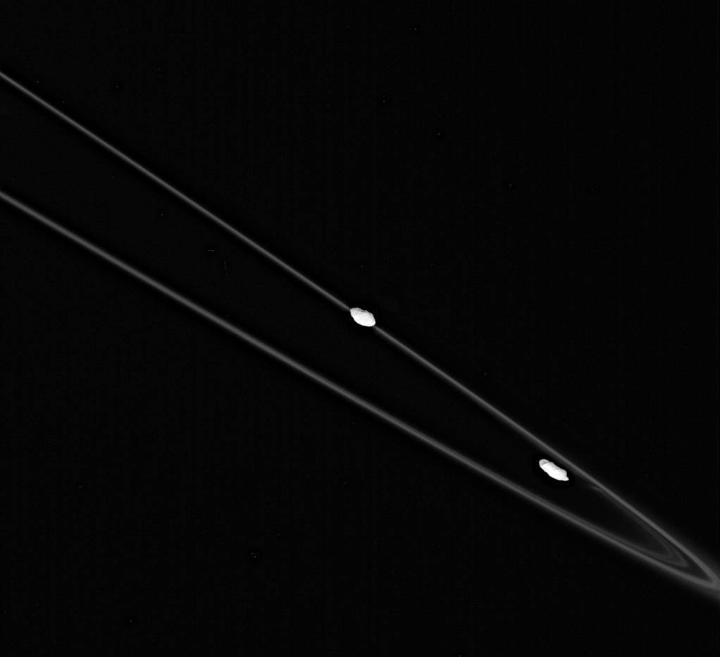 Black and white image of large, thin ring of Saturn with two small white moons circling