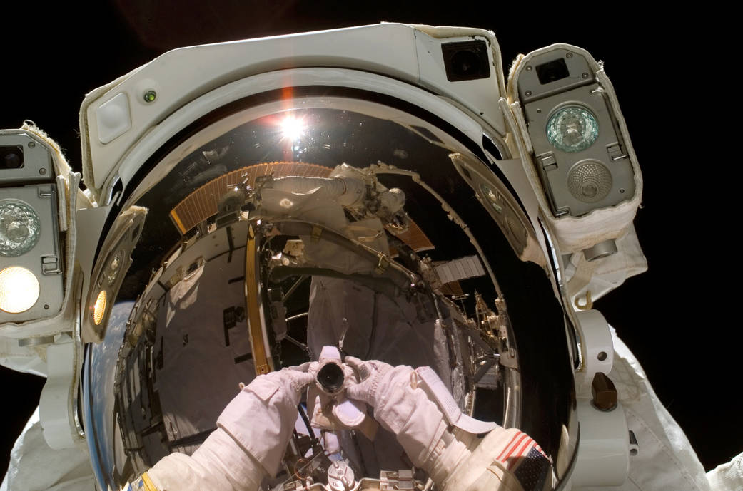 Closeup of astronaut helmet during spacewalk with reflection of camera